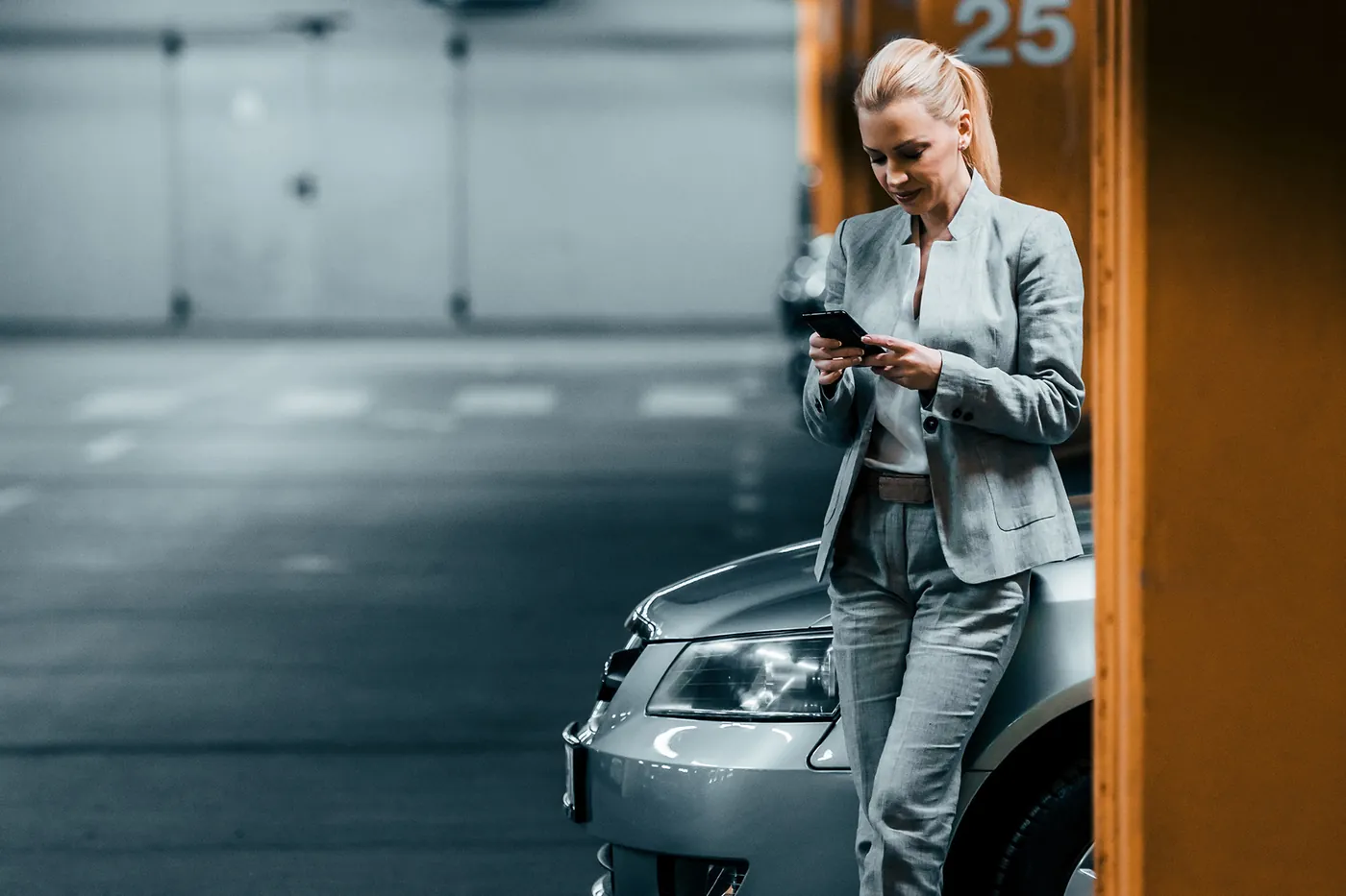 Manager checking a phone beside a company car in a parking garage